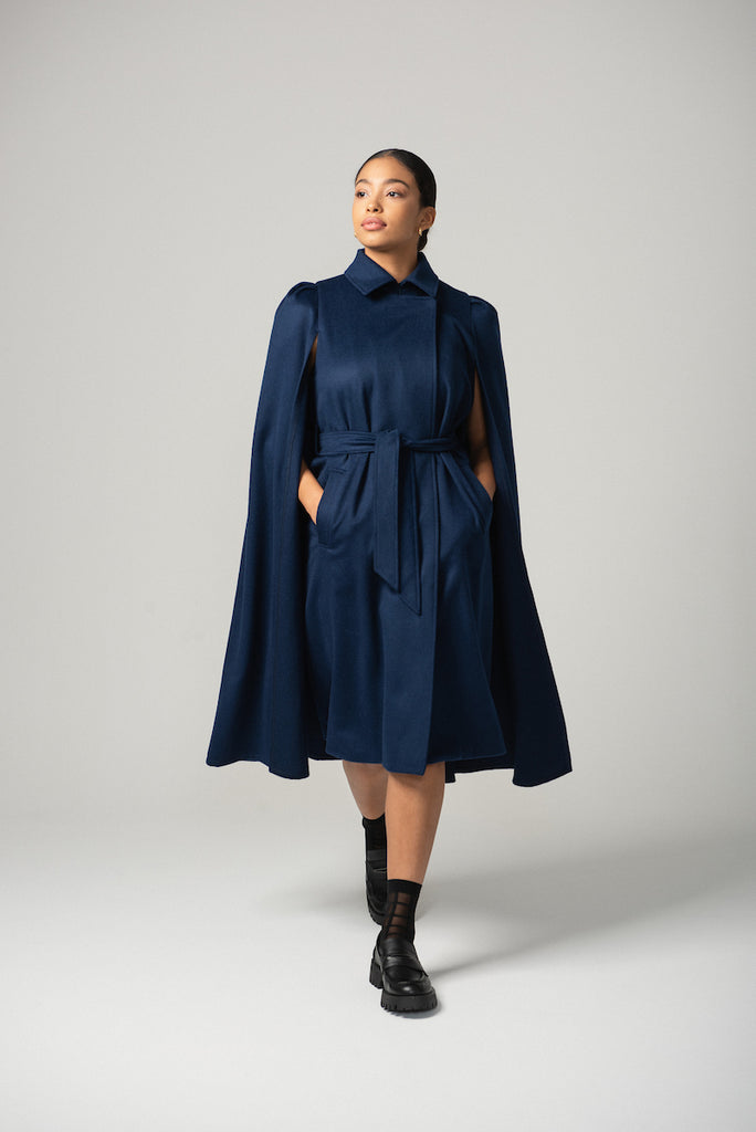 Woman wearing the Royal belted cape in navy with loafers and black socks. 